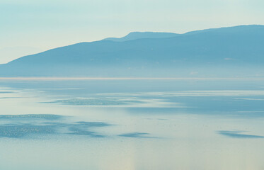 A minimalist and peaceful panoramic view of a calm lake with perfect reflections and a hazy mountain range on the distant horizon