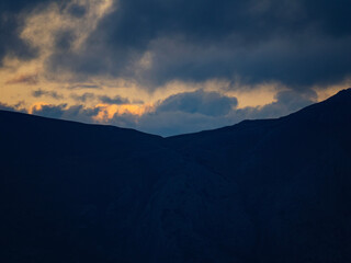 A beautiful and moody landscape of a dark mountain valley silhouette under a dramatic sky with golden sunset clouds