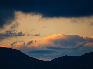 A stunning composition of a mountain silhouette with beautiful pink and golden clouds from a sunset above and dark clouds below