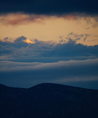 A beautiful vertical landscape of a dark mountain silhouette under a sky with layers of beautiful blue and golden clouds from a sunset