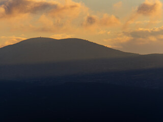 Obraz premium Detailed Close-up Photograph of Textured Orange and Golden Sunset Clouds hovering over Dark Rocky Mountain Slopes. Natural Contrast and Landscape Beauty at Dusk.
