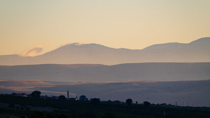 Obraz premium A minimalist and peaceful panoramic view of a calm lake with perfect reflections and a hazy mountain range on the distant horizon at sunset