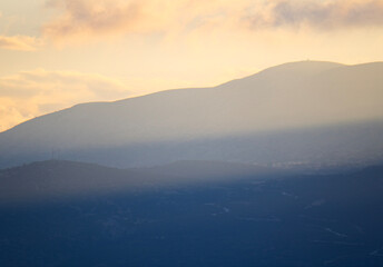 A beautiful hazy mountain landscape with soft golden light from the sunset creating a dreamy and atmospheric scene with layers of hills