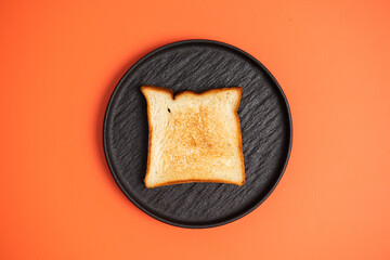Golden Brown Toast Slice on a Black Plate with Vibrant Orange Background