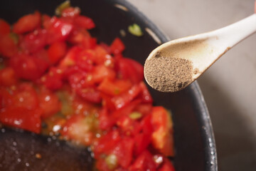 Cooking fresh tomatoes with spices in a kitchen setting