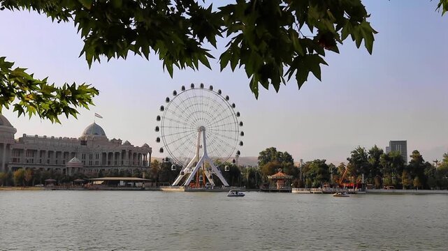 Scenic lakeside view of the Navruz Palace and Ferris wheel in Dushanbe, Tajikistan, showcasing the grand architecture and modern attractions under a clear sky