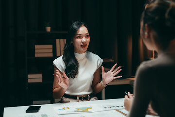 Young businesswoman sharing ideas and discussing project reports with colleague during a serious meeting at night office