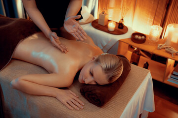 Fototapeta premium Caucasian woman customer enjoying relaxing anti-stress spa massage and pampering with beauty skin recreation leisure in warm candle lighting ambient salon spa at luxury resort or hotel. Quiescent