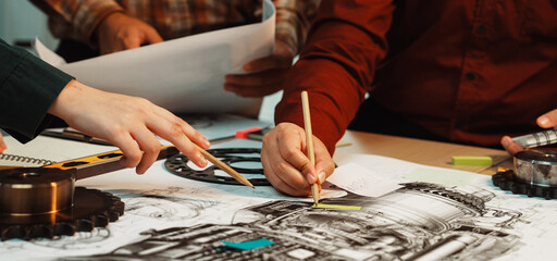 A group of engineers collaborates around a detailed technical drawing in an office setting, using...