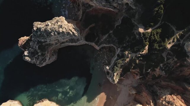 Overhead view from the drone reveals the intricate maze of Algarve&rsquo;s limestone cliffs and sea arches, with patches of green shrubbery and hidden coves below, as the drone advances