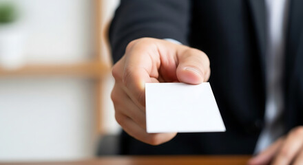 Close up of a businessmans hand extending a blank white business card forward.