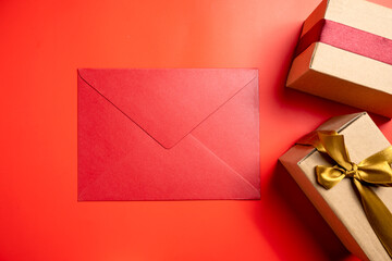Top view of brown gift box tied with golden and red ribbon with red envelope on colored background. Mockup or copy space. Concept of decoration for anniversaries, celebrations, presents, or surprises