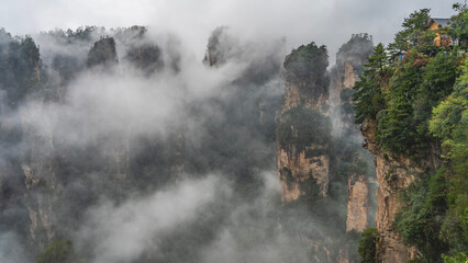 Mystical mountain landscape. The high cliffs  pillars are shrouded in fog. Peaks in the clouds. Green vegetation on steep slopes. China. Zhangjiajie National Forest Park. Avatar