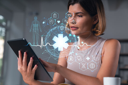 Smiling businesswoman in casual wear holding tablet device touching it at office workplace. Concept of distant work, business education, information technology. Health care icons hologram - Powered by Adobe