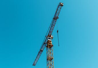 Naklejka premium A yellow tower crane on a construction site. Industrial machinery against a clear blue sky. Building and development concept with copy space