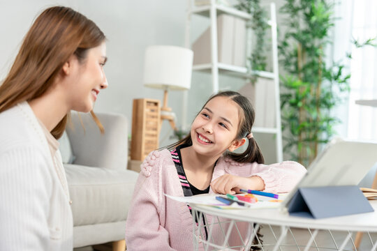 Asian loving mother support young kid daughter doing homework in house. 