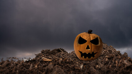 Closeup view of a Jack o' Lantern on the ground with dark and dramatic cloudscape background. The...