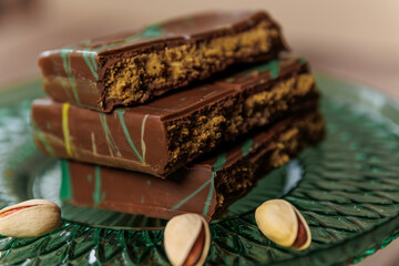 A bar of Dubai chocolate with dates, kadayif and pistachio paste with pistachios, on a green glass surface