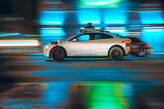 LOS ANGELES, CA - September 30, 2025: Google's Alphabet Waymo driverless self driving taxi cab driving along city street traffic at night. Blurred motion.