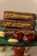 A bar of Dubai chocolate with dates, kadayif and pistachio paste with pistachios, on a green glass surface