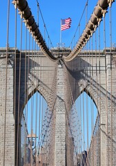 Obraz premium Brooklyn Bridge with American Waving Flag on top of Tower and blue sky