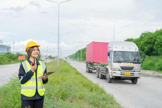Amidst the clatter of heavy cranes, a female engineer clutches her tablet, checking real-time data and recording maintenance schedules to prevent mechanical breakdowns. A delivery truck drives by. - Powered by Adobe