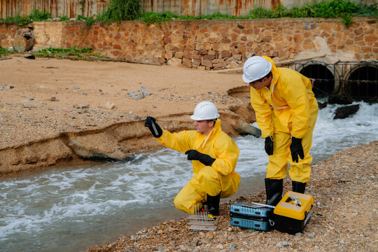 Team of environmental scientists in hazmat suits collecting water samples for pollution analysis and quality testing at an industrial wastewater discharge site.