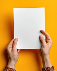 Blank white sheet of paper held by hands against an orange background