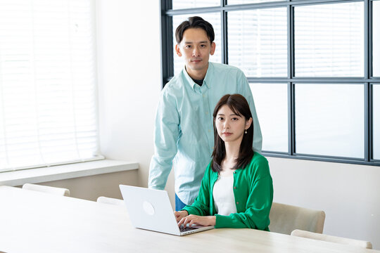 男性が女性にパソコン操作を教えている（または一緒に確認している）ビジネスシーン