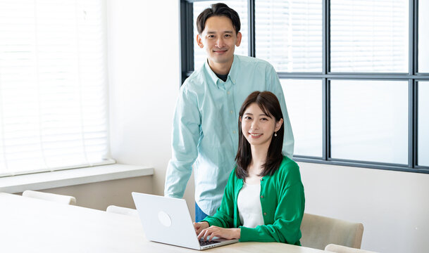 男性が女性にパソコン操作を教えている（または一緒に確認している）ビジネスシーン