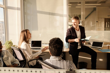 Multiethnic team of young creative office workers brainstorming in modern coworking space illuminated with bright sunlight