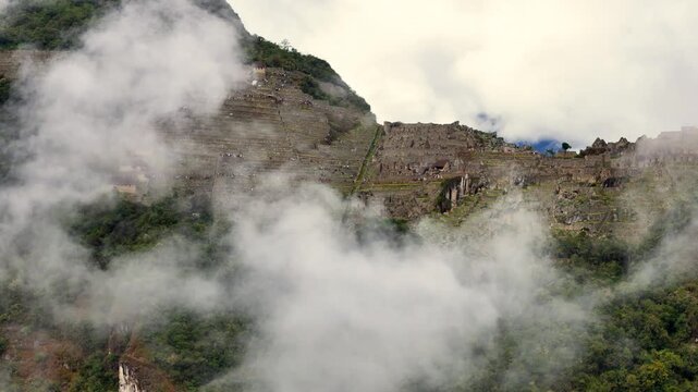 A cinematic drone shot starts with a close-up of the misty side of the Machu Picchu citadel and its terraces, then rises vertically to reveal a stunning top-down view of the entire ancient structure
