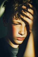 Thoughtful boy holding his head in dramatic light and shadow while struggling to study