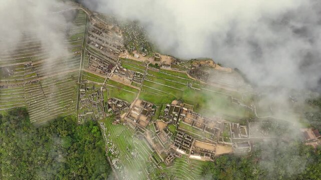 An epic and majestic drone shot begins with a close-up of the lush green terraces and structures of Machu Picchu, then soars upward, rising high above the clouds to reveal the immense scale