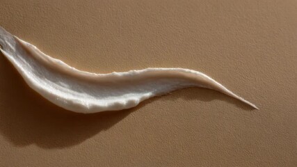 A lustrous off-white cream swatch with fine particles on a textured light brown surface casting a soft shadow - Powered by Adobe