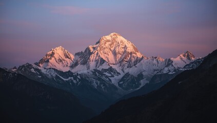 Obraz premium Majestic mountain range peaks, adorned with glistening snow, are illuminated by the soft, warm hues of the rising or setting sun, creating a breathtaking display of natural beauty.