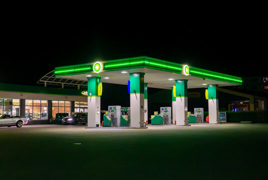 BP gas station at night with illuminated canopy, fuel dispensers and parked cars at square in Jarocin