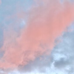 A dreamlike atmospheric scene where a dramatic mass of pink and peach clouds glows against a pale mauve and blue sky during sunset or sunrise, filling the frame with pastel colors.