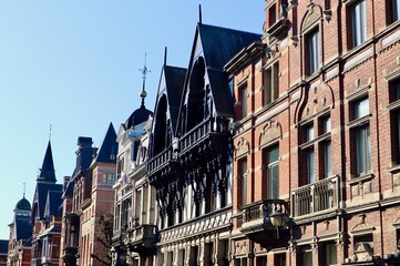 Historic European townhouses: one half-timbered style, the other red brick Neo-Renaissance, featuring intricate gables against a clear blue sky in Antwerp, Belgium