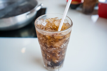 Close-up of a glass filled with iced cola and a straw on a white tabletop in a restaurant setting