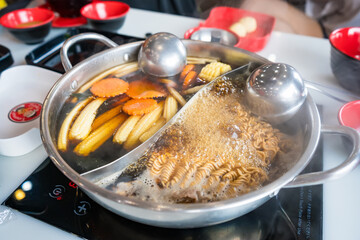 Close-up of a traditional Asian hot pot meal with vegetables and broth boiling in a divided metal pot on a tabletop burner