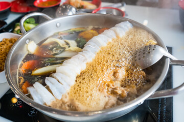 Close-up of a hot pot dish with shrimp, vegetables, and meat boiling in broth at an Asian restaurant with diners in the background
