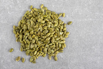 Hulled pumpkin seeds on gray background, top view
