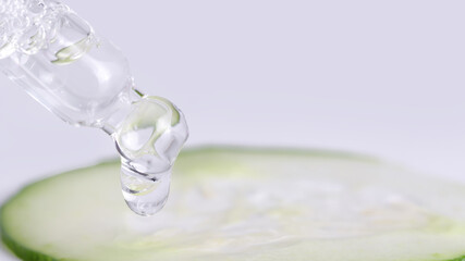 Dropper and droplet in focus, cucumber slice blur, clean beauty product concept, 16:9.