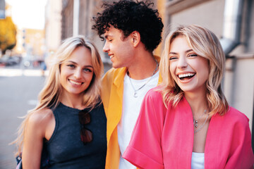 Group of young three stylish friends posing in the street. Fashion man and two cute female dressed in casual summer clothes. Smiling models having fun. Cheerful women and guy outdoors