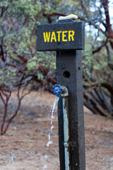 Rustic campground water spigot with flowing stream and wooden sign