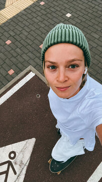 Young woman  rides a skateboard wearing green beanie on urban street