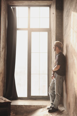 Man standing by a large window in a rustic room during daytime