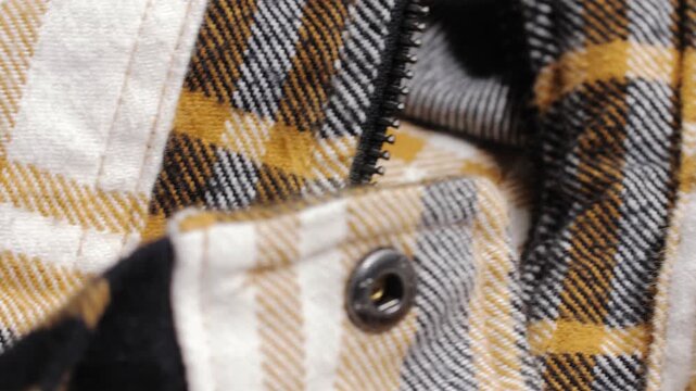 A mustard, black and white plaid flannel jacket reveals zipper and stitch details during a slow macro pan