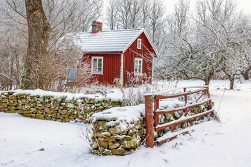 Red gate by a stone wall to a red wooden cottage in a wintry landscape © Lars Johansson